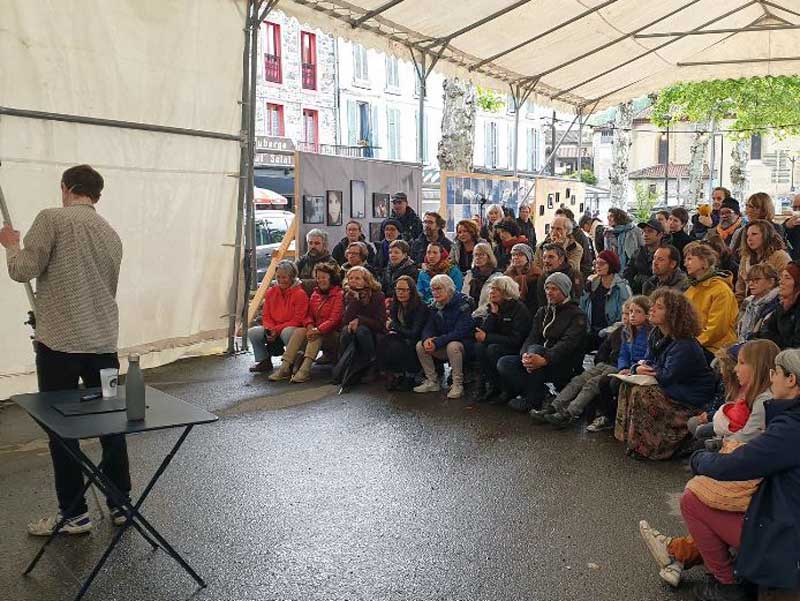 Un homme intervient face à un public de tous âges, dans le cadre d'une animation culturelle en Ariège.